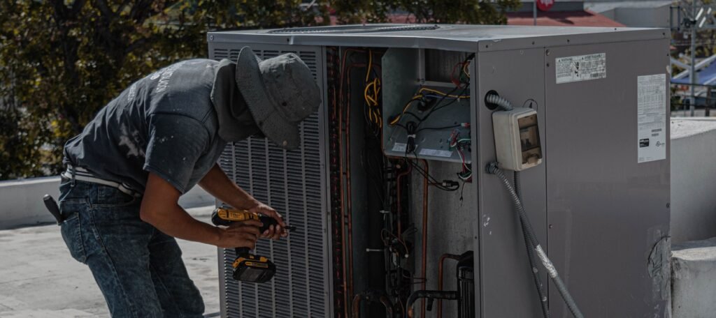 Technician using a power drill to repair an outdoor air-conditioning unit.