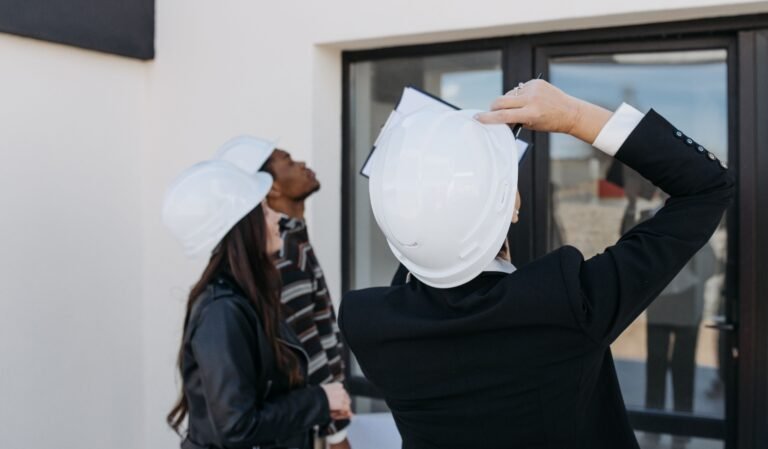 Property professionals wearing hard hats inspecting a modern building exterior.