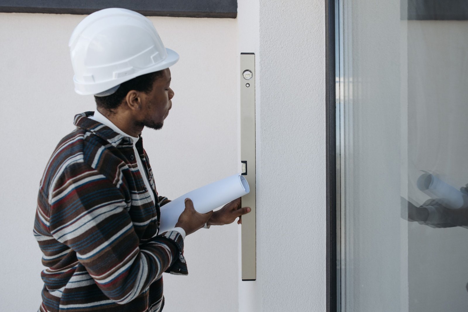 Construction inspector wearing a hard hat uses a spirit level to check the alignment of a building wall.