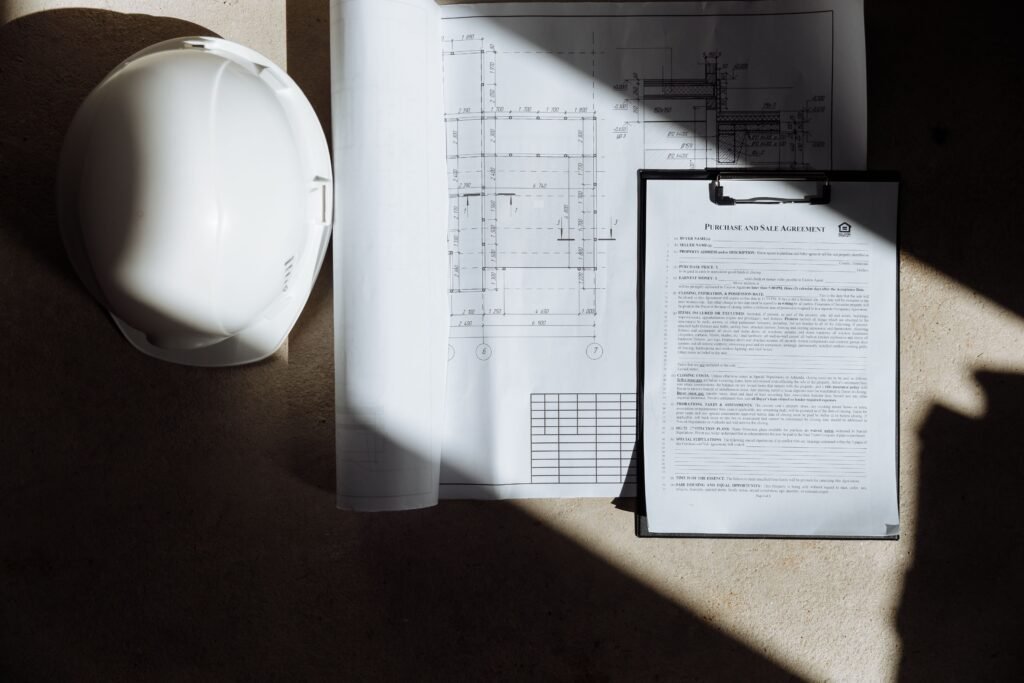 Construction plans, a hard hat and a property purchase agreement arranged on a desk.