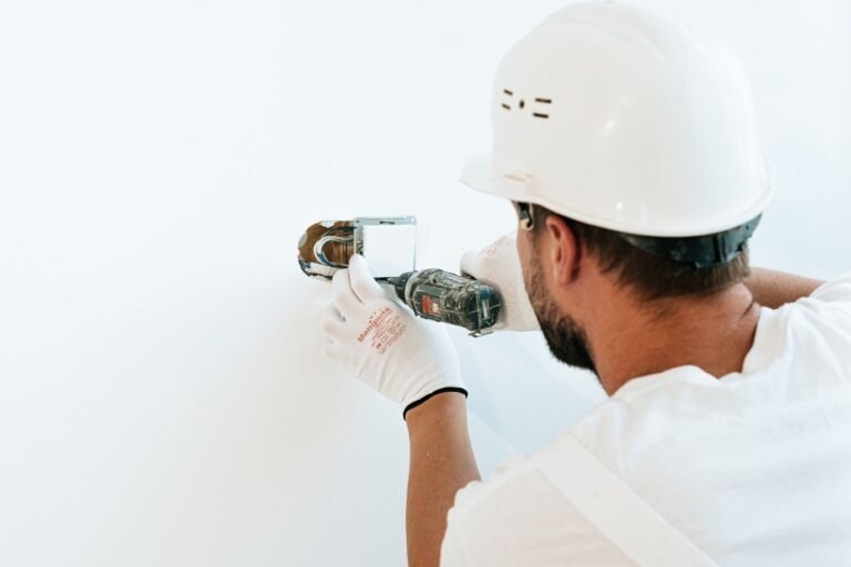 Construction worker wearing helmet and gloves uses a power tool to fix a wall