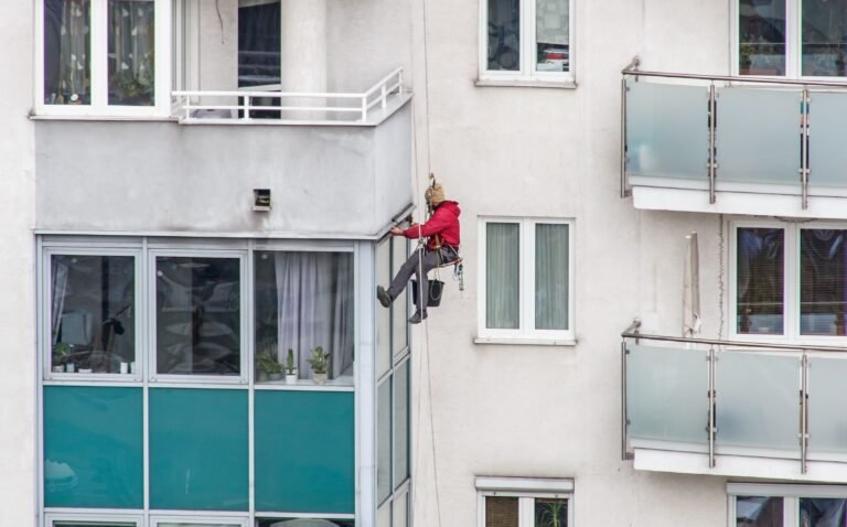 Professional window cleaner scaling a modern residential building with glass balconies